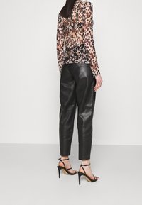 Haut à manches longues transparent avec motif léopard, associé à un pantalon en cuir noir et à des sandales à talons hauts noires à lanières. Textures lisses et design moulant.