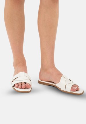 Sandales à glissière en cuir blanc avec un design de bande croisée, semelle plate et accents beiges subtils. orteils visibles et esthétique minimaliste.