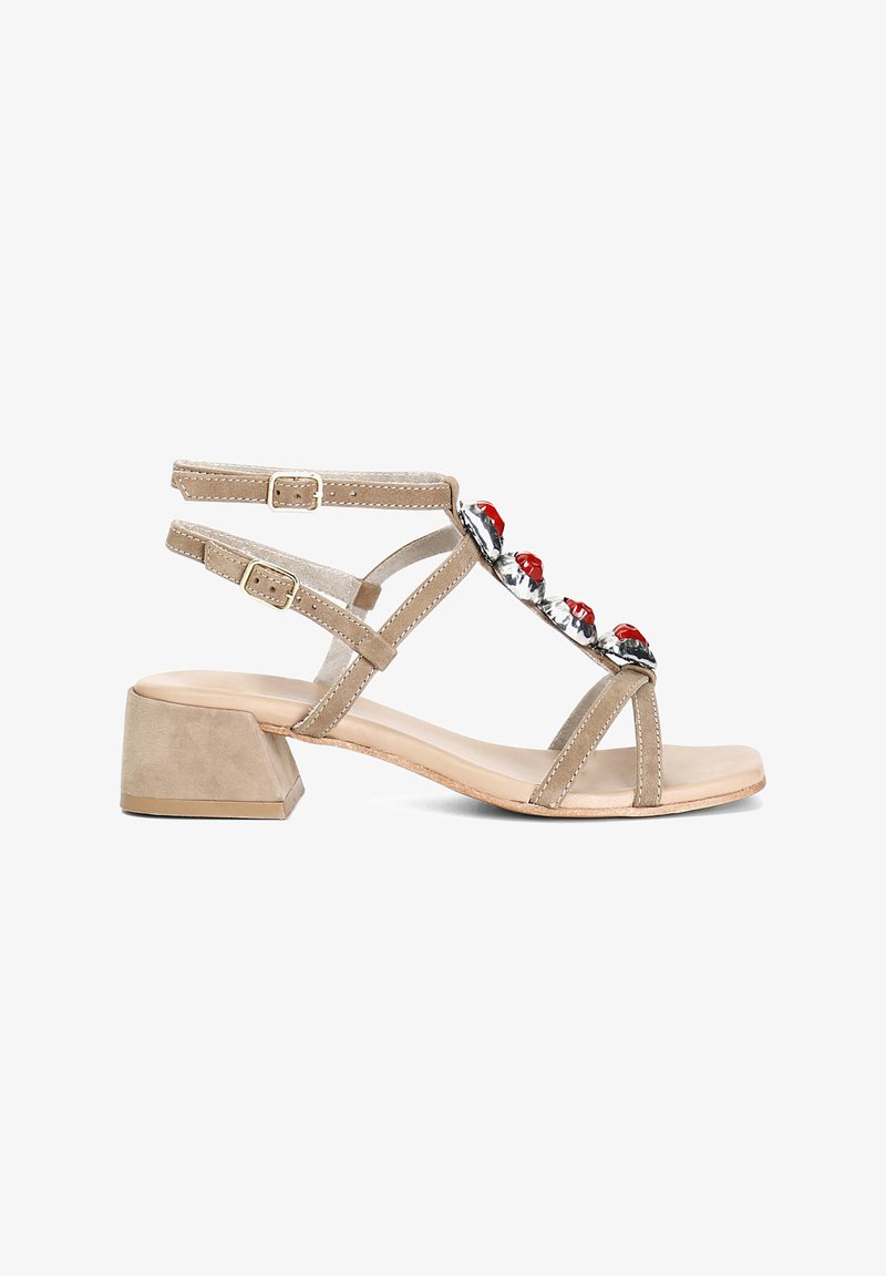 Beige suede korot kengät, joissa on paksu kantapää, useita hihnoja ja punaisia jalokiviä etuosassa. Sileä nahkainen pohja.