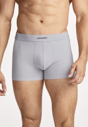 Man wearing light gray Jockey boxer briefs, standing with arms relaxed against a plain white background.