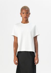 T-shirt blanc à manches courtes avec un col rond, fabriqué en tissu lisse. Porté avec une jupe noire, avec une coupe droite et des détails minimaux.