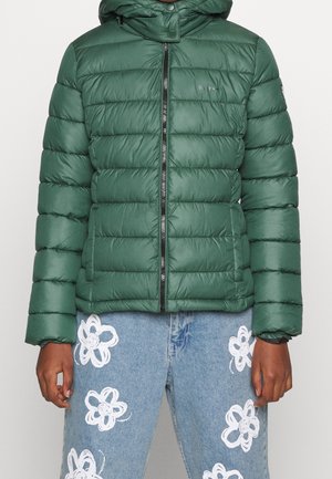 Doudoune verte avec capuche, dotée de sections matelassées horizontales, d'une fermeture éclair à l'avant et de poignets élastiques. Jean à motifs avec des fleurs blanches.
