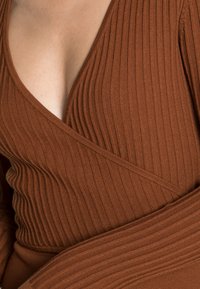 Top castanho com nervuras e decote em V profundo, apresentando um design envolvente e tecido texturizado. Material suave e elástico com mangas longas.