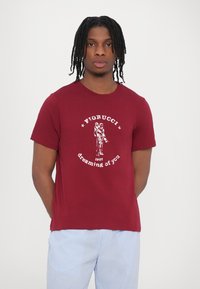Burgundy cotton T-shirt with rounded neckline, featuring white graphic print and text “Fiorucci 1967 dreaming of you” centered on the front.