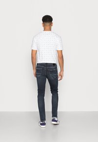 Witte korte mouwen shirt met een klein zeilbootpatroon, gecombineerd met donkerblauwe slim-fit jeans en witte sneakers met paarse accenten.