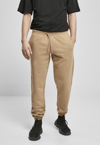 Beige joggebukser med elastisk midje og mansjetter, med sidelommer og snøring, sammen med svarte treningssko.