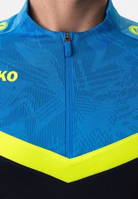 Maglia da ciclismo blu con un motivo testurizzato, dettagli gialli, zip di un quarto di lunghezza e una sezione inferiore nera. Logo visibile sulla spalla.