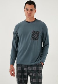 Hosszú ujjú türkiz színű póló mintás mellszámmal; kockás szürke és fekete nadrággal párosítva. Puha anyagtextúra.