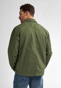 Olive green cotton jacket with a structured collar, side pockets, and button cuffs. Features a plain back and a relaxed fit.