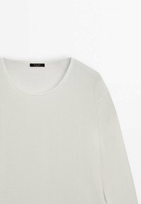 Pull blanc à manches longues avec col rond, texture fine en maille et petite étiquette noire à l’intérieur du col.