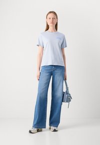 Lys blå bomulls T-skjorte med teksttrykk, kombinert med vide blå jeans og en liten blå håndveske. Fottøyet inkluderer grå joggesko.
