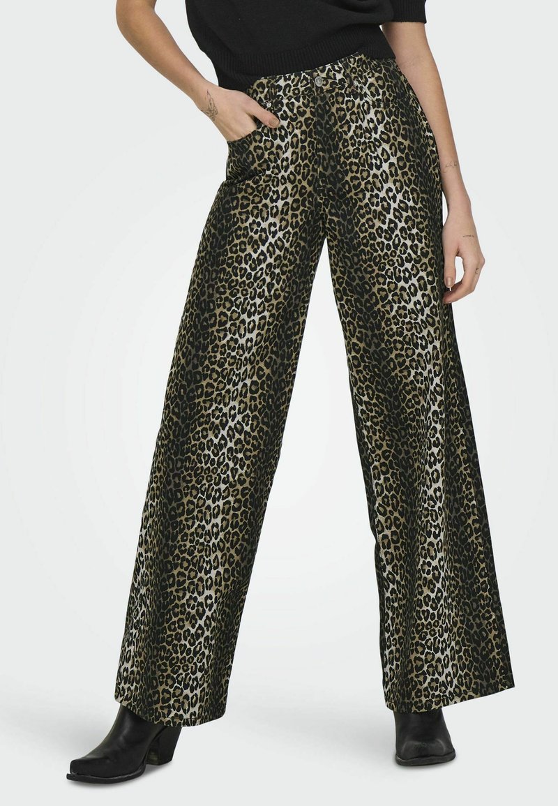 Pantalons larges en imprimé léopard en tissu doré et noir brillant. Dotés d'une taille haute et de poches, associés à des bottes à talons noires.