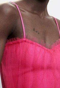 Vestido de tul rosa con finos tirantes de spaghetti y cuerpo texturizado, que presenta un forro transparente y suaves volantes en capas en el escote.