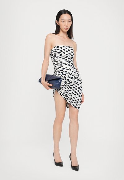 Strapless mini-jurk in wit met zwarte stippen, gerimpelde stof, asymmetrische zoom, gecombineerd met een navy textuur clutch en zwarte hakken.