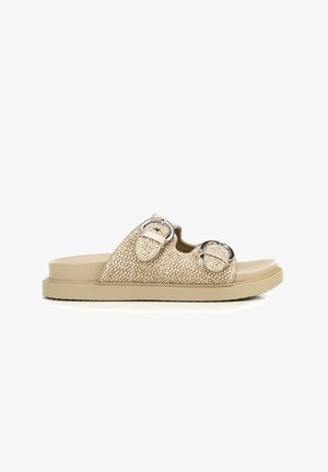 Beige woven slide sandal with two adjustable silver buckles and a flat rubber sole, shown from the side on a white background.