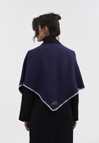 Tumši zils šalle ar viļņotu baltu apdari, kas rotāta ar ziedu izšuvumiem. Mīksts audums eleganti krīt pār pleciem.