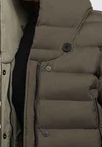 Olivgrüne, puffige Jacke mit Reißverschluss, schwarzen Druckknöpfen und Kapuze. Der Stoff hat eine glatte Textur mit gestepptem Isolationsmaterial.