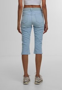 Pantaloni capri in denim azzurro chiaro con vita media, cinque tasche e una texture liscia e aderente, abbinati a scarpe da ginnastica neutre.