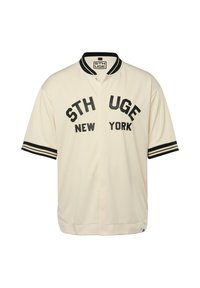 Maglietta da baseball a maniche corte di colore crema con lettering nero "STHUGE NEW YORK" e maniche a righe nere. Tessuto leggero e testurizzato.