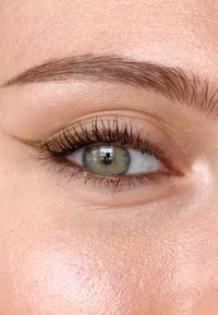 Primo piano di un occhio con iride verde e marrone, lunghe ciglia scure e un eyeliner dorato in evidenza, su una pelle di tono chiaro.