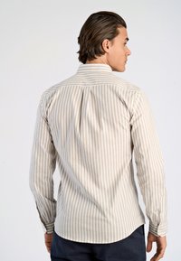 Valkoinen beige raitapaita, jossa on tavallinen kaulus, pitkät hihat, napitettavat hihansuut ja kaareva helma. Sileä rakenne; hienovarainen pystysuora kuvio.