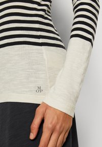 Randig långärmad topp i marinblått och krämigt, med avslappnad passform, lätt stickad och en liten broderad logotyp vid fållen.