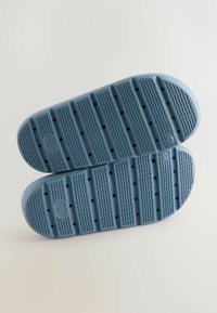 Sål af blå sneakers, gummimateriale, struktureret overflade med riller og cirkulære huller til trækkraft. Rundede kanter og fladt design.