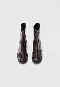 Bottes mi-mollet en cuir verni marron avec une silhouette élancée, finition brillante et semelles épaises en caoutchouc noir. Présente des détails de fermeture éclair sur les côtés.