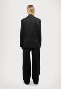 Czarna dopasowana marynarka o prostym kroju, zestawiona z szerokimi spodniami. Gładka faktura, minimalistyczne detale i wyraźna sylwetka.