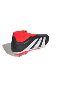 Botín de fútbol negro con un collar de tipo calcetín rojo, que presenta tres franjas blancas y una parte superior texturizada. Suela rosa con tacos moldeados.