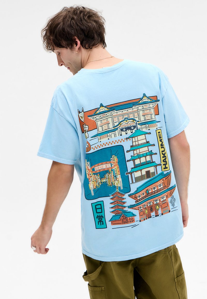 Light blue cotton t-shirt featuring a colorful, graphic print of Asian architecture and symbols on the back. Relaxed fit, short sleeves.