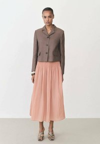 Giacca cropped marrone con colletto a bavero, abbinata a una gonna fluida color pesca fino al ginocchio e scarpe in stampa pelle di serpente texturizzata.