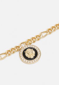 Gold chain bracelet featuring a circular pendant with a lion's head design, black background, and surrounded by clear rhinestones.