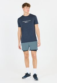 Marineblaues Sport-T-Shirt mit dem Aufdruck "ENDURANCE" in Weiß, kombiniert mit hellgrauen Shorts und dunkelblauen Sneakers, dazu weiße Knöchelsocken.