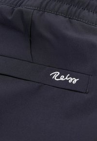 Tengerészkék anyag, texturált felszínnel, hímzett "Reiss" címkével egy varrott pánton. Simaság és rugalmas derékpánt.