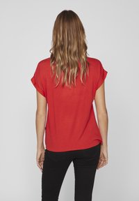 Maglietta rossa a maniche corte con vestibilità rilassata, texture morbida e maniche arrotolate. Indossata con jeans skinny neri, mostra uno stile casual visto da dietro.