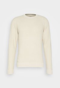 Krämfärgad stickad tröja med ett strukturerat mönster, rund hals, och ribbade muddar och nederkant. Har raglanärmar för en avslappnad passform.