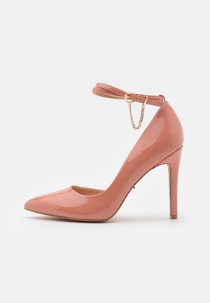 Kiiltävä vaaleanpunainen stiletto-korkokenkä, jossa on terävä kärki ja nilkkaremmi, jossa pieni kultainen solki ja koristeellinen ketju.