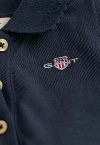 Námořnické polo tričko s texturovanou tkaninou, dvěma zlatými knoflíky a vyšívaným logem v bílé a červené barvě. Detailní límec s jemným prošíváním.