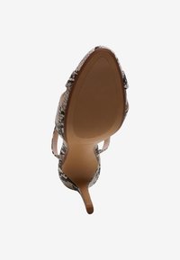 Vue inférieure d'une chaussure à talon haut unique avec un motif imprimé serpent et une pointe pointue sur fond blanc.