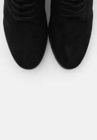 Schwarze Wildlederschuhe mit runder Zehenform, ausgestattet mit Schnürsenkeln und dezenten Nähdetails. Glatte Textur mit einer flachen Gummisohle.