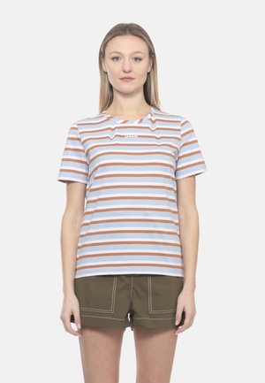 Donna che indossa una t-shirt a righe bianche e marroni a maniche corte e pantaloncini color verde oliva con cuciture bianche, in piedi contro uno sfondo bianco semplice.