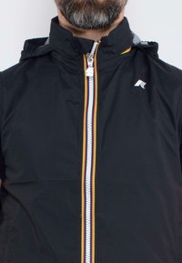 Giacca nera impermeabile con zip, caratterizzata da una striscia multicolore lungo la chiusura e un logo sulla parte superiore sinistra. Cappuccio integrato.