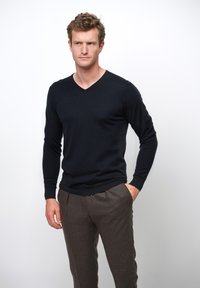 Svart v-ringad tröja av ett slätt, lätt material, kombinerad med bruna skräddarsydda byxor med en subtil textur och smal passform.