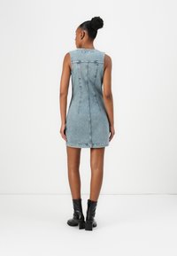 Denim ermløs kjole, lyseblå, tettsittende silhuett, sømdetaljer bak, underkant som faller midt på låret, brukt med svarte hælboots.