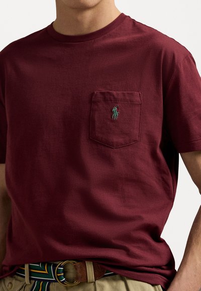 Burgundy bomullströja med rundad hals och bröstficka. Har en grön broderad logotyp, korta ärmar och en avslappnad passform.
