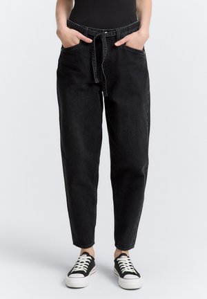 Schwarze Jeans mit hoher Taille, lockerer Passform, zwei Fronttaschen und einem Stoffgürtel. Kombiniert mit schwarzen Leinenschuhen.