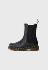 Bota Chelsea de couro preto com painéis laterais el�ásticos, acabamento texturizado, costura amarela e uma sola de borracha durável e ligeiramente transparente.