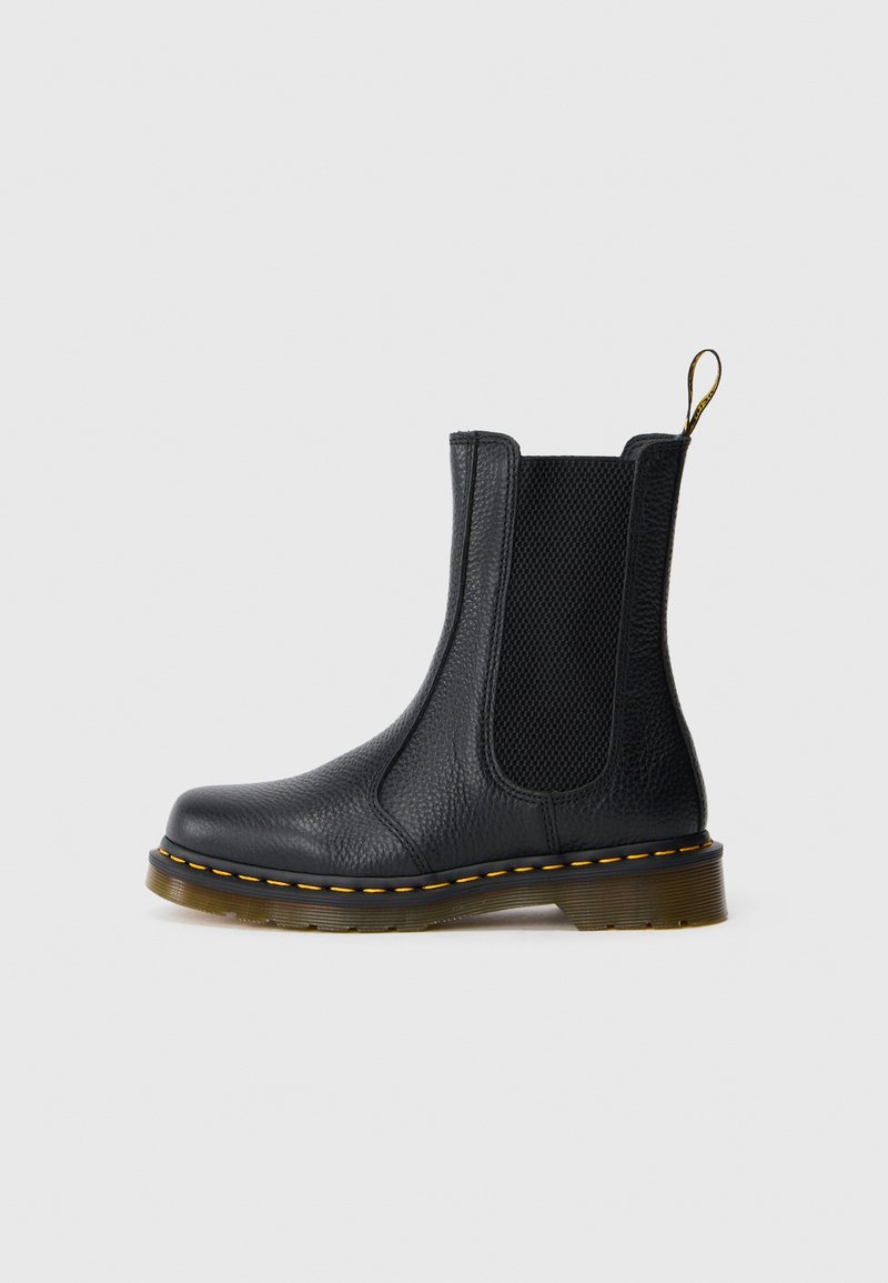 Bota Chelsea de couro preto com painéis laterais elásticos, acabamento texturizado, costura amarela e uma sola de borracha durável e ligeiramente transparente.