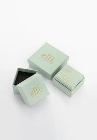 Twee mintkleurige sieraaddozen met gouden letters. Eén doos is open en onthult een zwarte binnenkant. De kleinere doos is gesloten.
